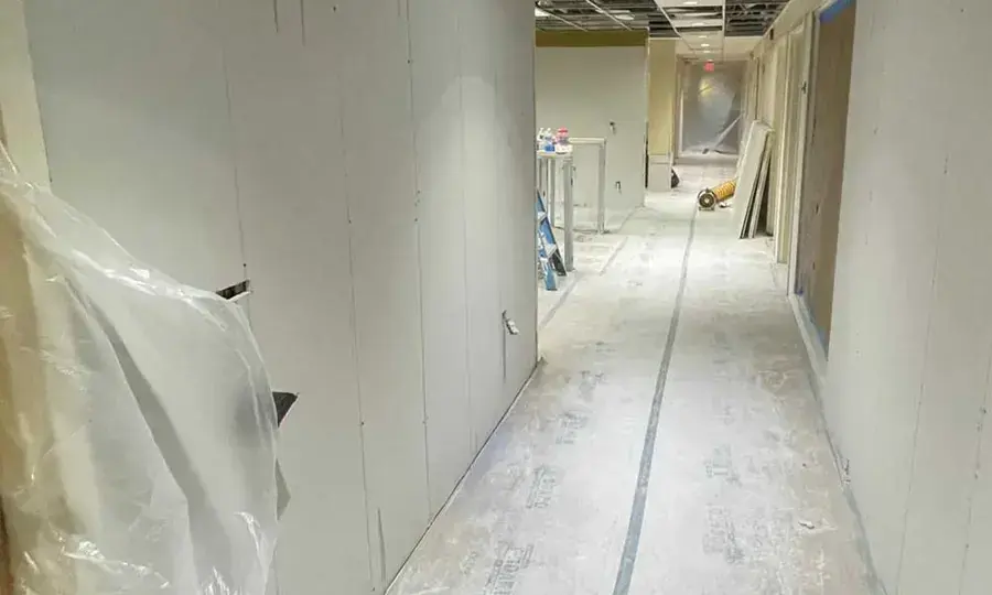 Plastic containment and cut wall bottoms along a hallway during structural drying in a Garden City home