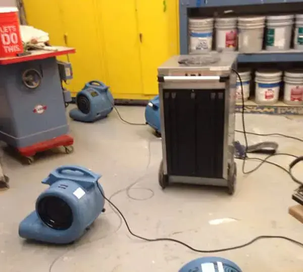 Dehumidifier and air movers drying a basement workshop floor after a water loss