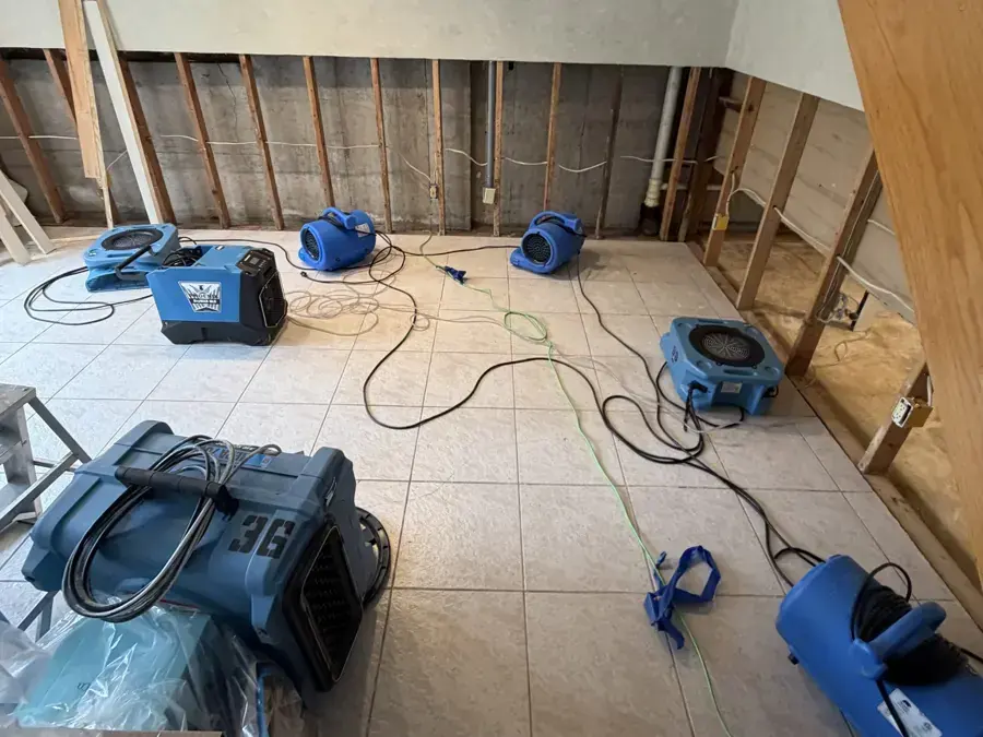 Air movers and an LGR dehumidifier drying a gutted room on a tile floor
