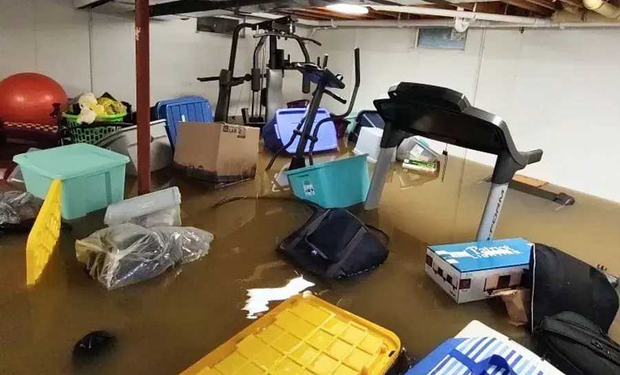Flooded basement with stored bins, boxes and exercise gear floating in standing water in a Hempstead area home