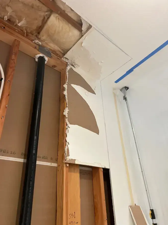 Ceiling and wall opened to expose a drain pipe and the framing above after an interior leak