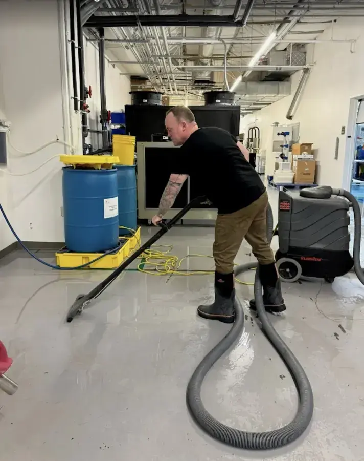 Technician extracting water from the floor of a commercial lab space with a dehumidifier running