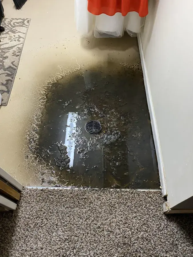 Dark sewage water spreading across a basement floor around a backed-up floor drain
