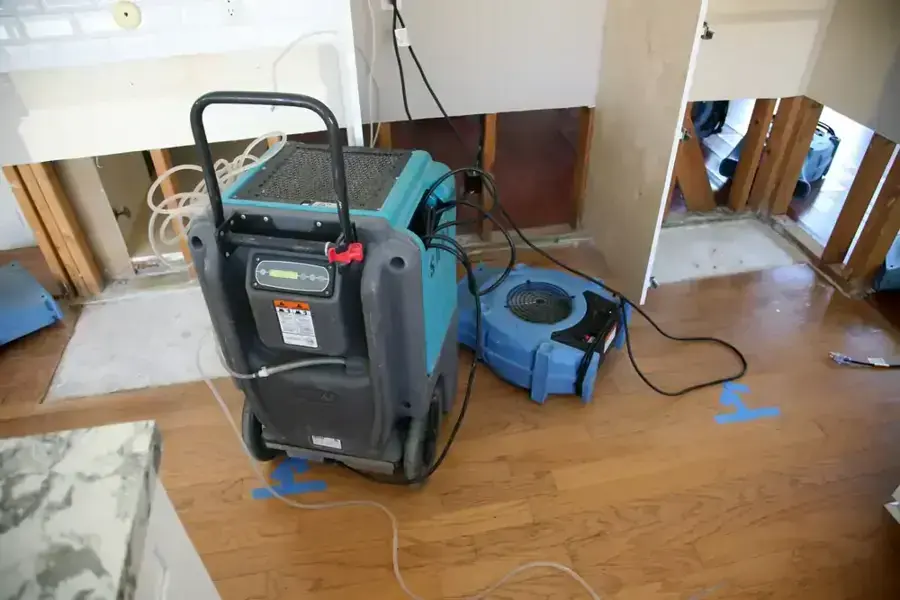 Dehumidifier and air movers drying a hardwood floor with the wall bottoms cut away
